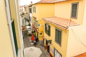 A narrow street with yellow buildings, a red umbrella, and a sign for a restaurant. - Apartamentos Taberna (Funchal)