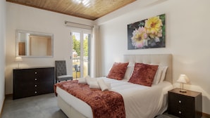 A bedroom with a bed, a dresser, a nightstand, a mirror, and a painting of flowers. - Apartamentos Taberna (Funchal)