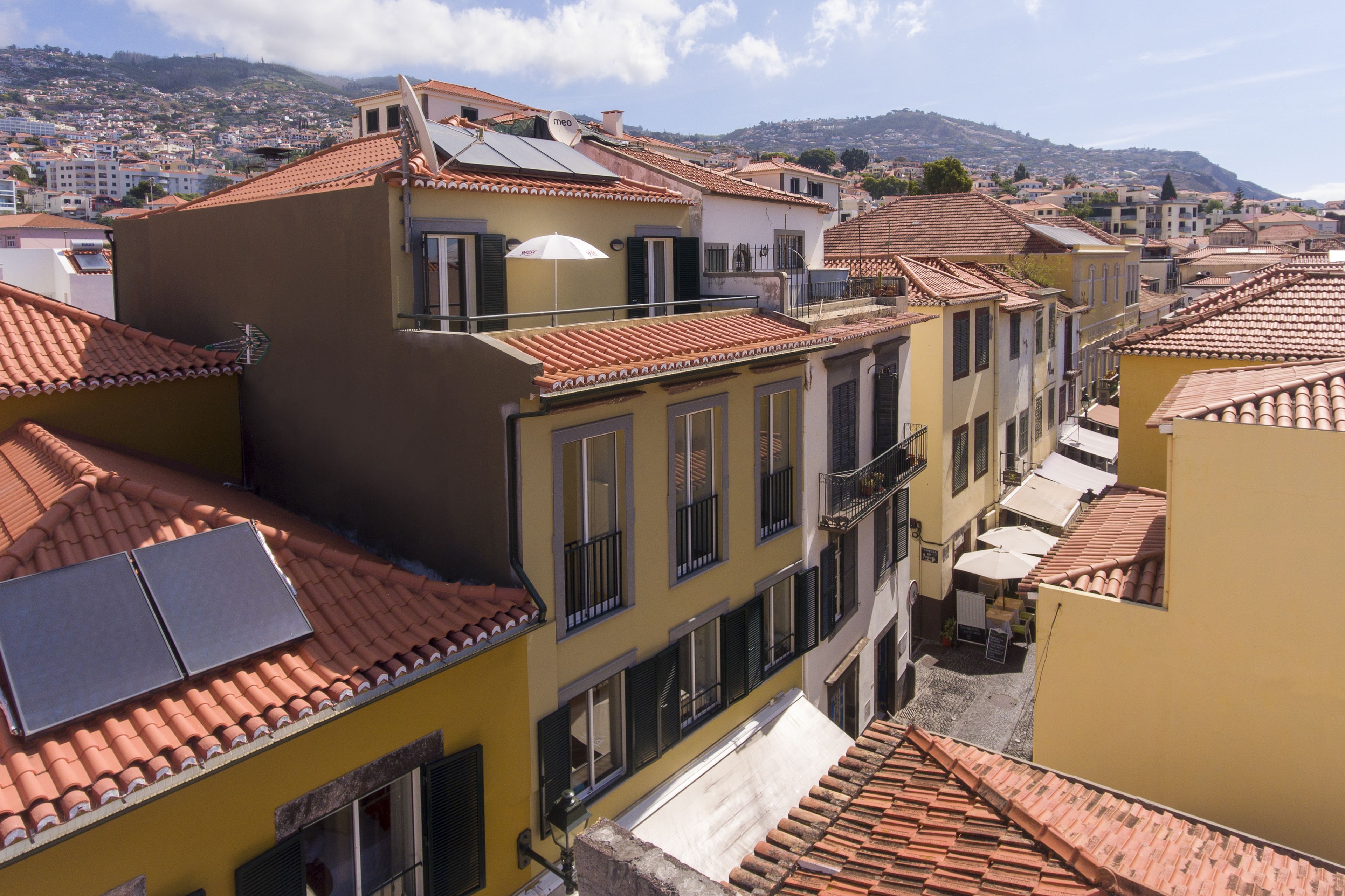 A row of yellow buildings with red-tiled roofs and balconies, featuring solar panels and outdoor seating areas.