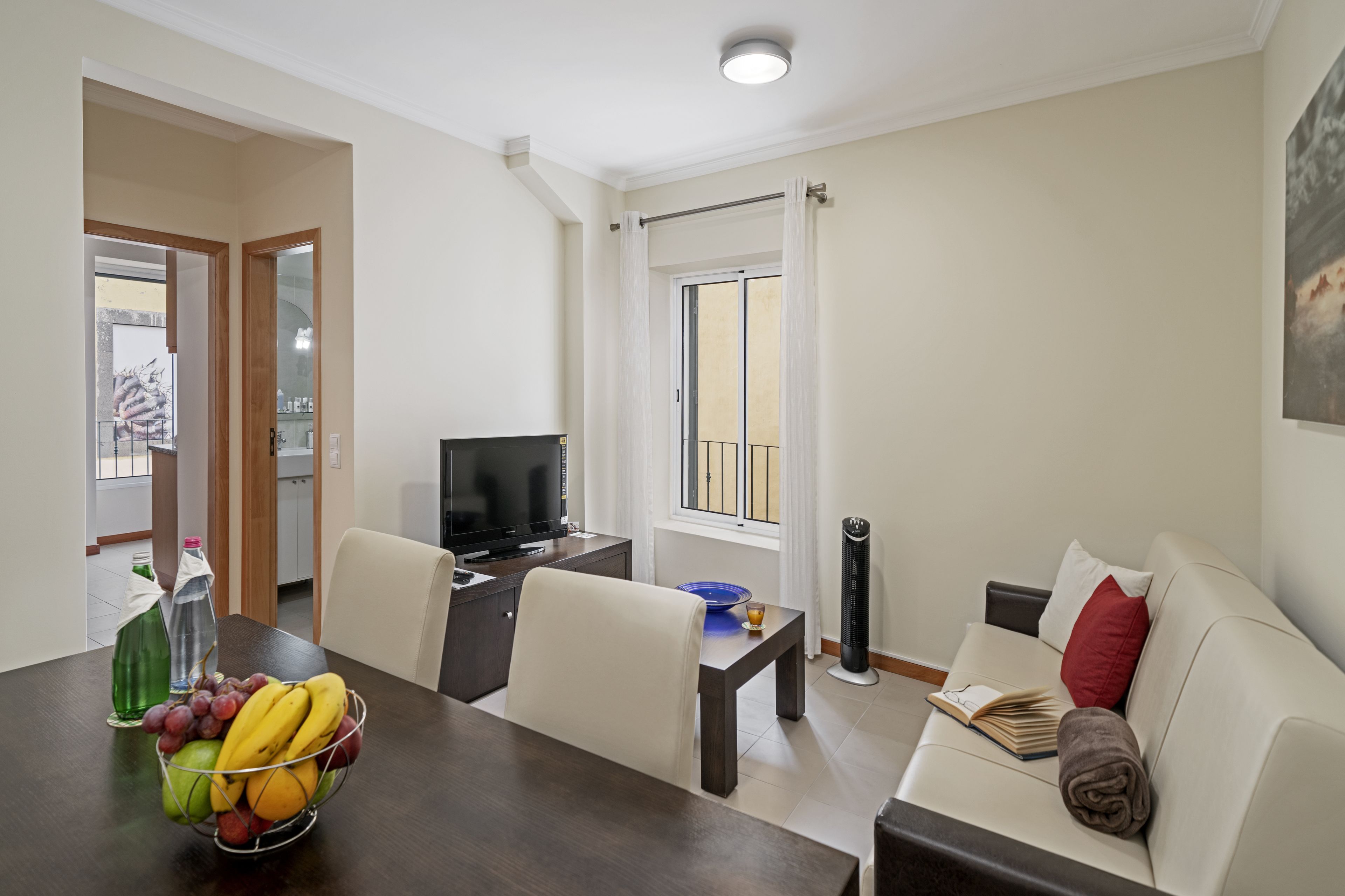 A modern living room with a dining area, a flat-screen TV, a sofa, and a balcony with a view.