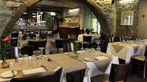 A restaurant with stone arches, tables set for dining, and a bar in the background. - Apartamentos Taberna (Funchal)