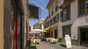 A narrow street with outdoor seating, buildings with shutters, and a clear sky. - Apartamentos Taberna (Funchal)