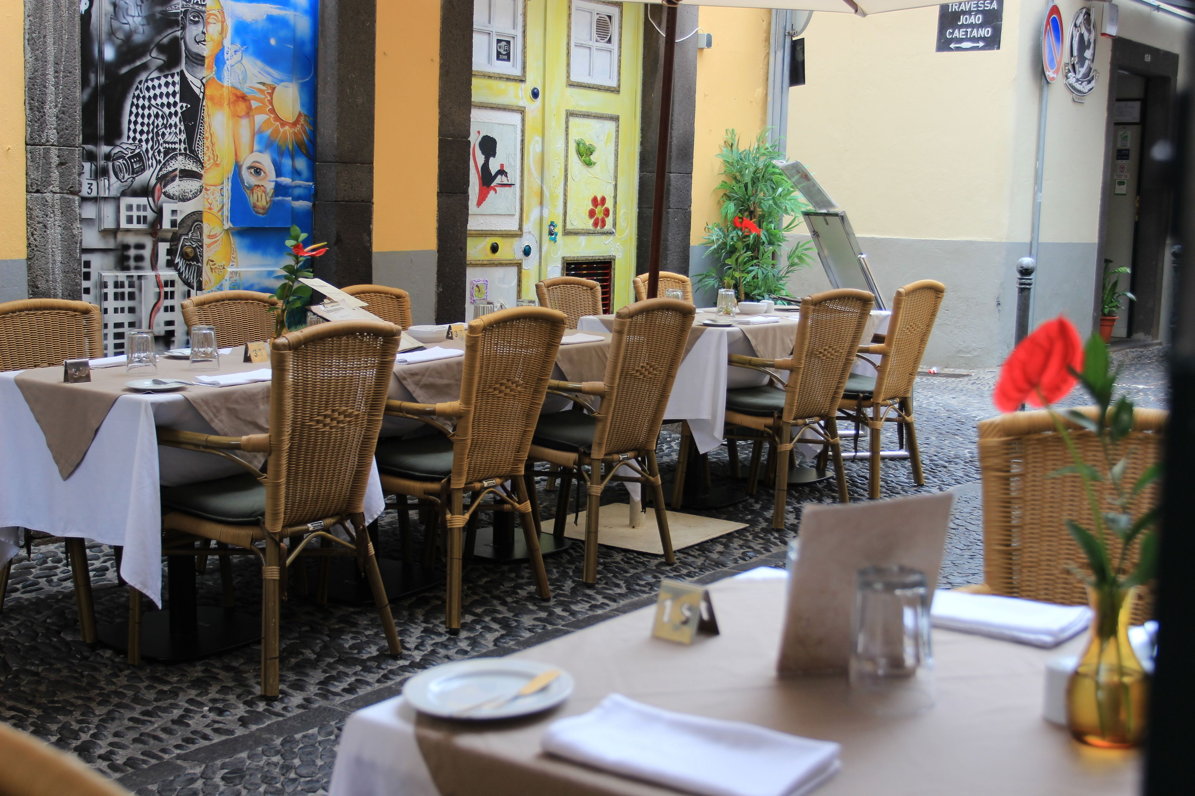 A restaurant with wicker chairs and tables, a tiled floor, and a mural on the wall.
