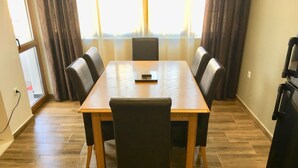 A conference room with a wooden table and black chairs, a window with curtains, and a refrigerator on the right. - DayDream (Pomorie)