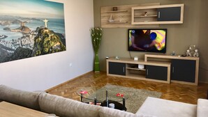 A modern living room with a large TV, wooden entertainment unit, and a scenic painting. - DayDream (Pomorie)