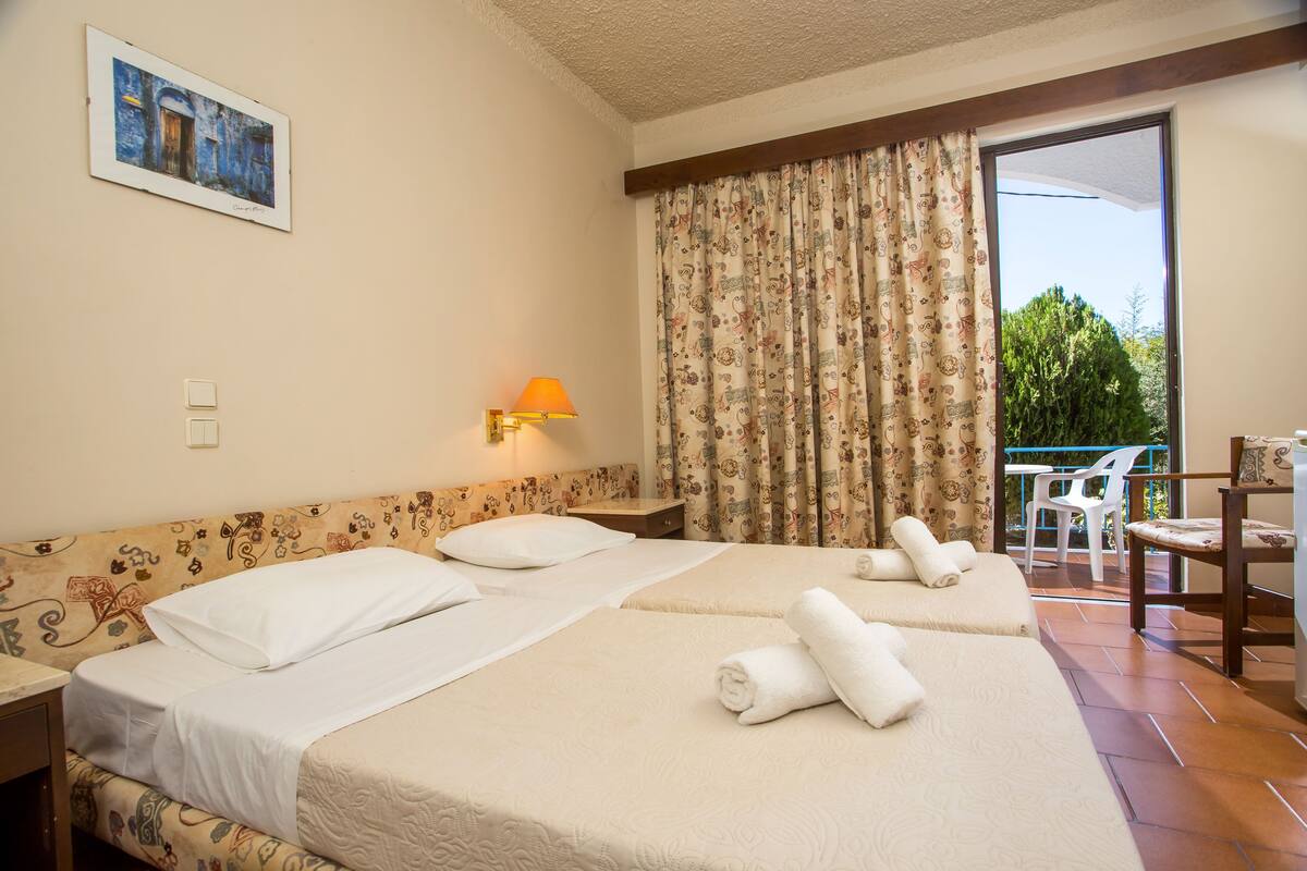 A hotel room with two beds, a balcony with a chair, and a painting on the wall.