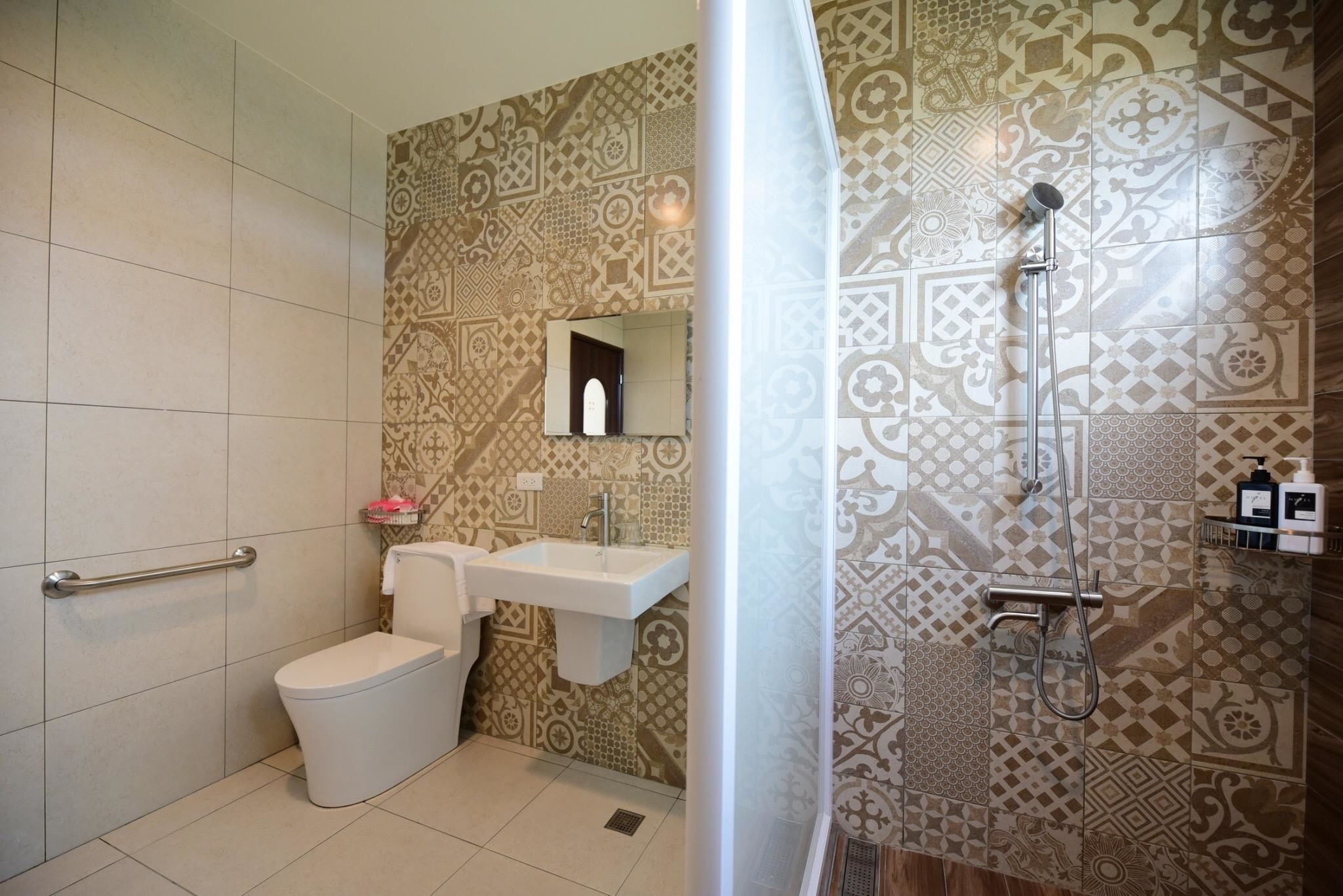 A bathroom with patterned tiles, a white toilet, a sink, and a shower.