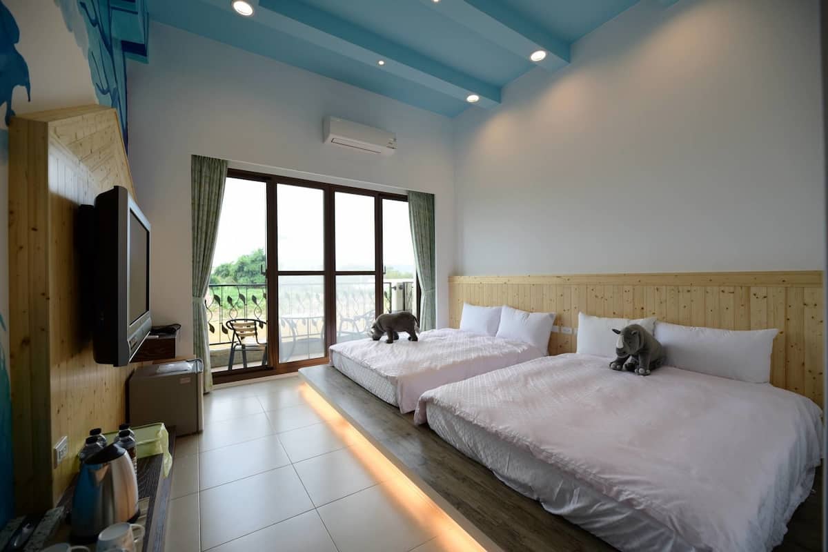 Habitación de hotel con dos camas, televisión, cafetera y balcón con vistas.