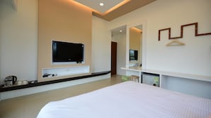 A modern hotel room with a large bed, a flat-screen TV mounted on the wall, a small desk with a chair, and a mirror above the desk. - Yasengawa (Hengchun)