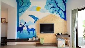 A room with a large TV mounted on a wooden wall, a bench, a small table with a cat, and a wall mural of deer and trees. - Yasengawa (Hengchun)