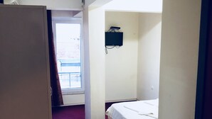 A small hotel room with a single bed, a television mounted on the wall, and a window with a view of the outside. - Hotel Sarayevo (Ayvalik)