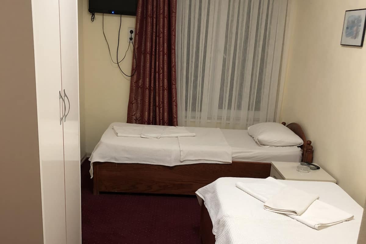 A hotel room with two single beds, a wardrobe, a television mounted on the wall, and a curtain.