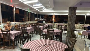 An outdoor dining area with checkered tablecloths, wooden chairs, and a stone pillar. - Hotel Sarayevo (Ayvalik)
