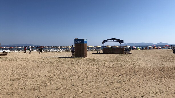 A beach with a wooden structure labeled "Kabin" and several beach umbrellas. - Hotel Sarayevo (Ayvalik)