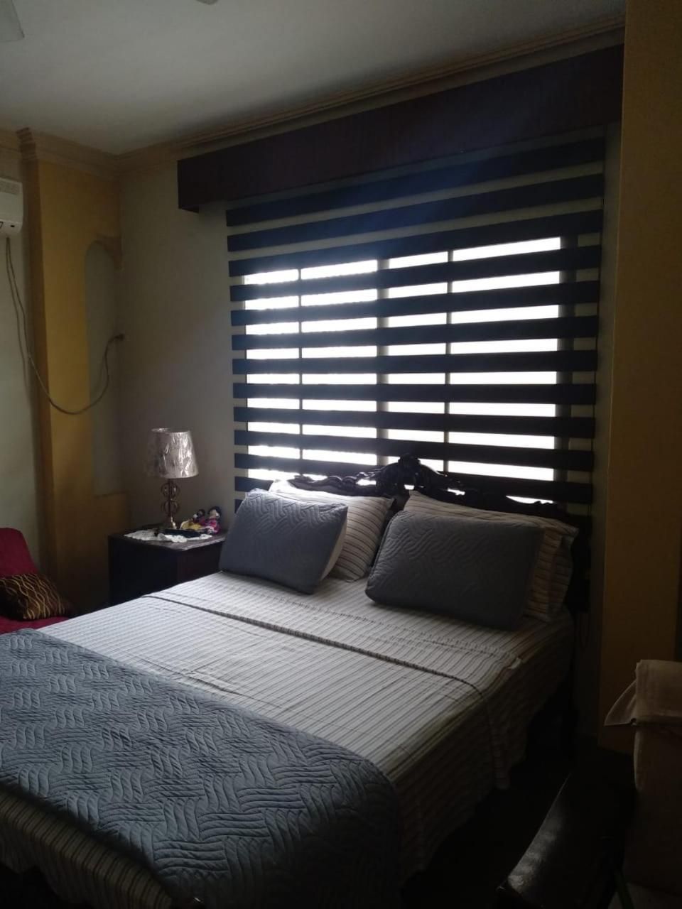 Une chambre à coucher avec un lit, une table de chevet, une lampe et une fenêtre avec des stores.