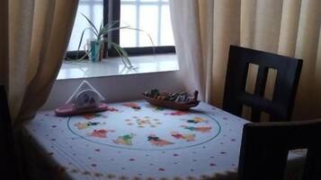 A dining table with a floral tablecloth, a small plant on the windowsill, and a chair.