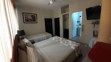 A hotel room with a bed, a desk, a chair, a television, and a ceiling fan.