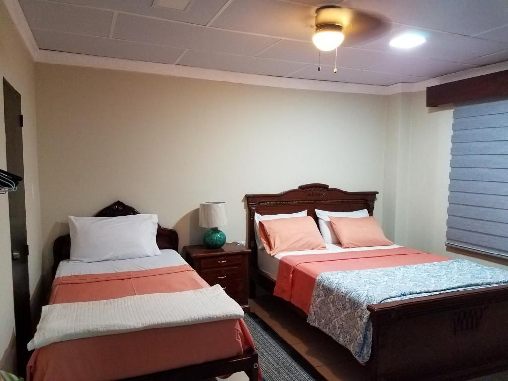 Habitación de hotel con dos camas, una mesita de noche, una lámpara y un ventanal con persianas.