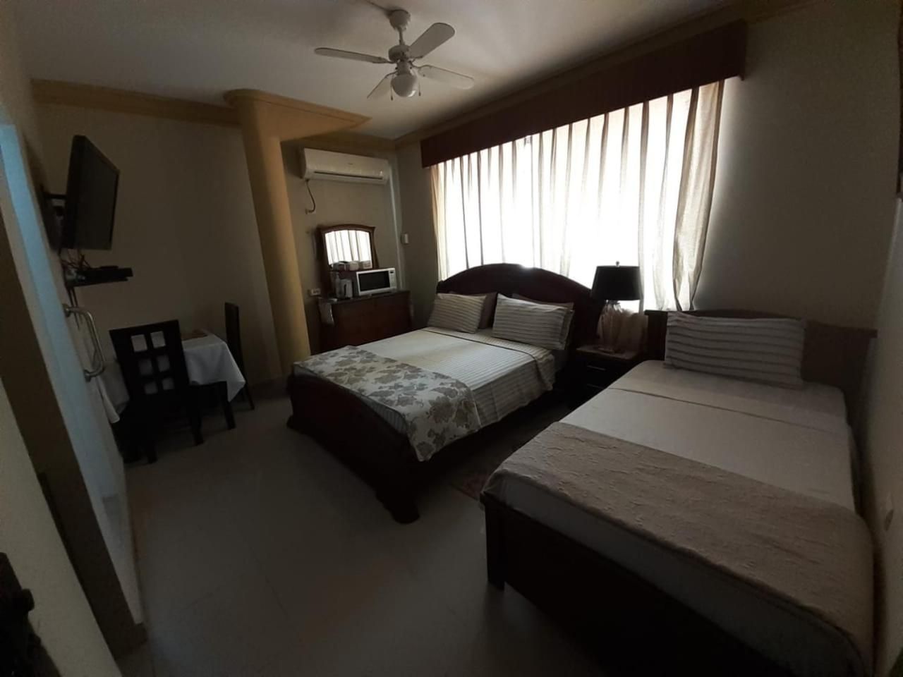 Una habitación de hotel con dos camas, un ventilador de techo, un televisor y un escritorio con una silla.