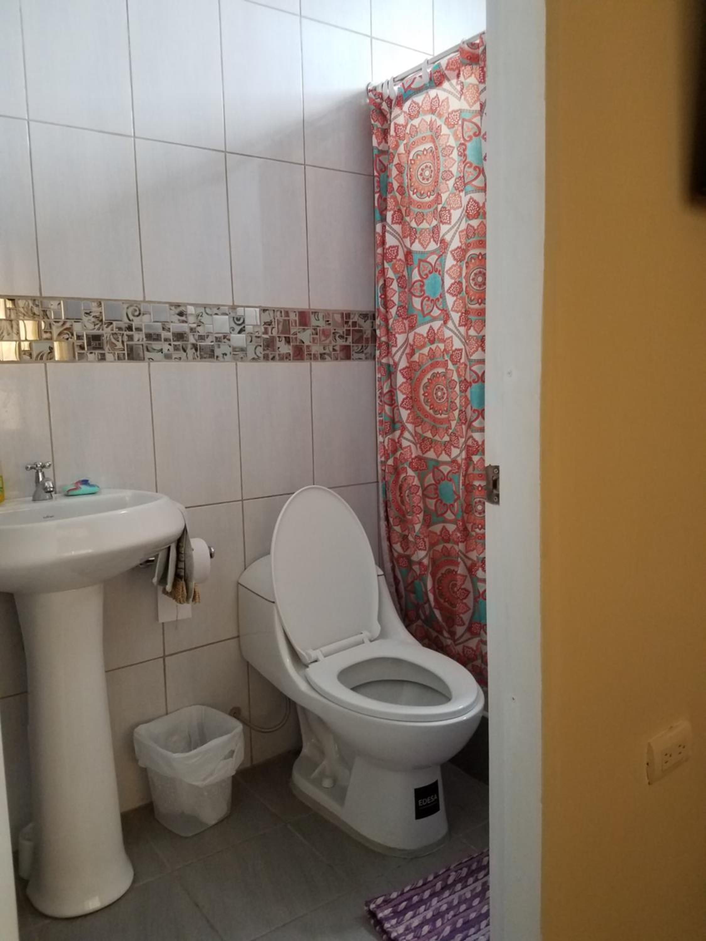 Un baño con lavamanos blanco, inodoro y cortina de ducha estampada.