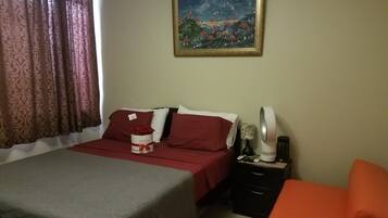 A bedroom with a bed, a nightstand, a chair, a painting, and a window with curtains.