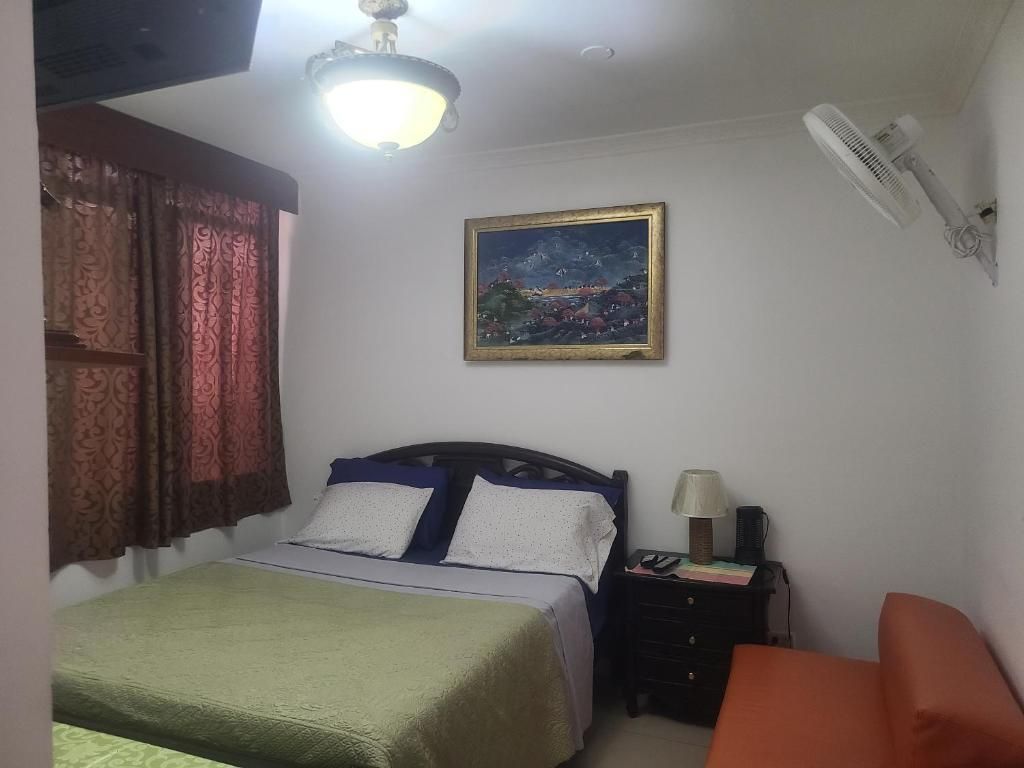 A bedroom with a bed, a nightstand, a lamp, a painting, and a ceiling fan.