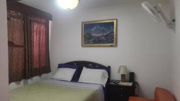 A bedroom with a bed, a nightstand, a lamp, a painting, and a ceiling fan.