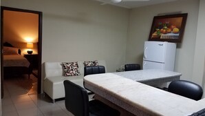 A compact hotel room with a bed, a small sitting area with a sofa and chairs, a dining table with chairs, a ceiling fan, and a refrigerator. - Casa Serena (Guayaquil)