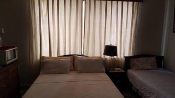 Een hotelkamer met een bed, nachtkastje met lamp, televisie en een dressoir.