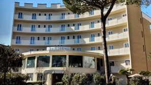 A multi-story hotel with a curved facade, balconies, and a central entrance with a canopy. - Hotel Schiller (Cervia)
