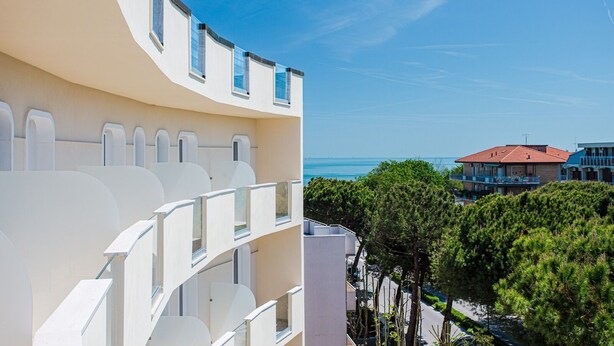 A modern building with a curved facade, multiple balconies, and a view of the sea and other buildings. - Hotel Schiller (Cervia)