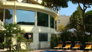 A swimming pool with lounge chairs, surrounded by a building with balconies and large windows. - Hotel Schiller (Cervia)