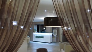 A modern hotel lobby with a reception desk, seating area, and a large chandelier. - Hotel Schiller (Cervia)
