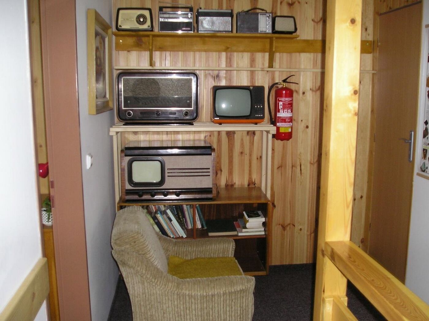 Une pièce avec un mur en bois, une bibliothèque contenant divers objets, un téléviseur et une chaise.