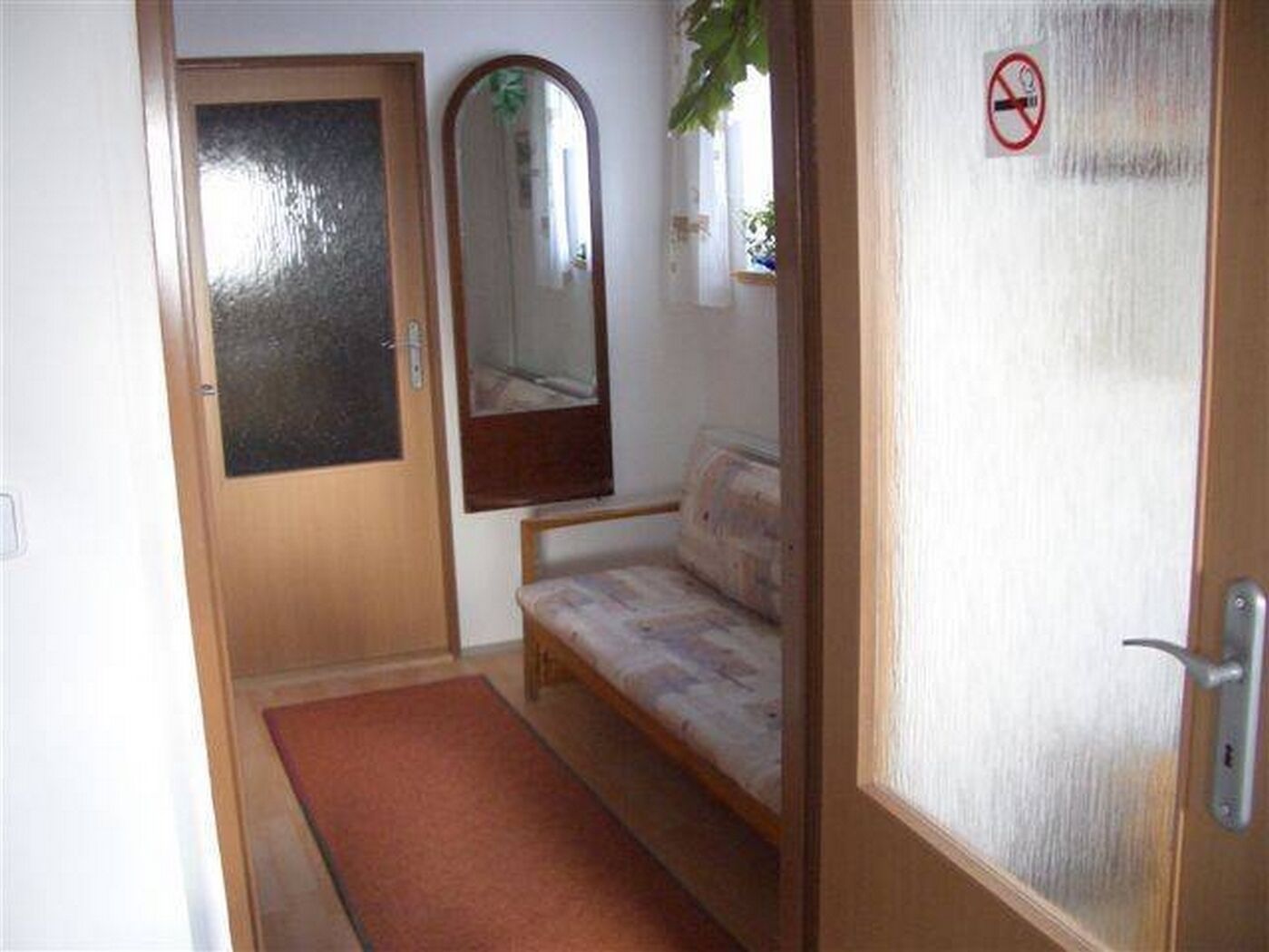 Um quarto com porta de madeira, um espelho, um sofá e um tapete vermelho.