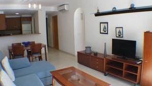 A modern living room with a sofa, coffee table, TV, and a dining area with chairs and a table.