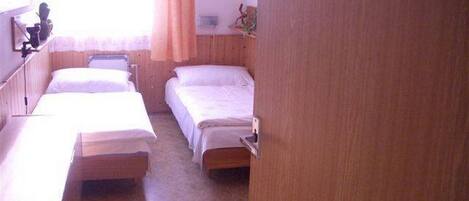 A room with two single beds, a wooden desk, a chair, a small table, and a window with curtains.