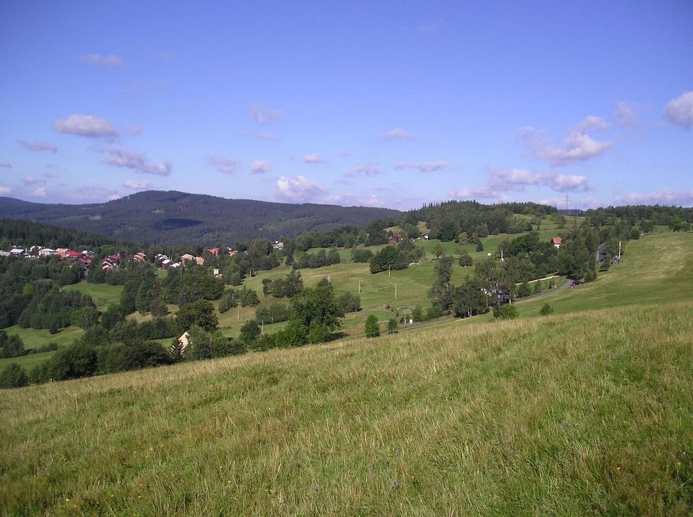 Un paysage rural caractérisé par des collines douces, des maisons dispersées et un ciel bleu dégagé.