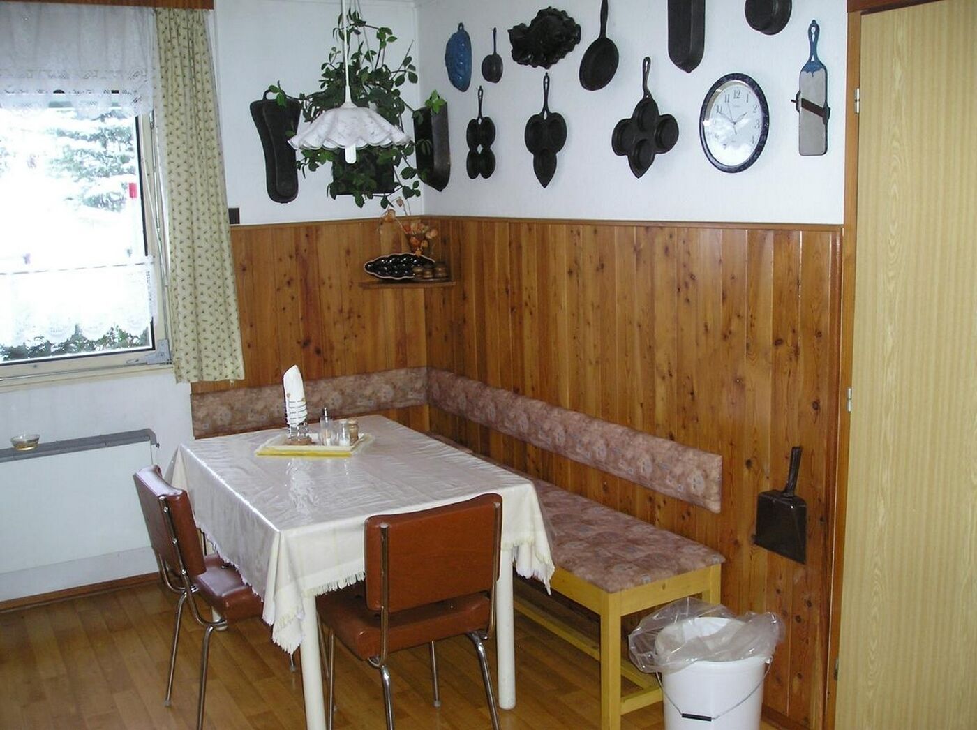 A small dining area with a table set for two, a bench, and a wall-mounted clock.