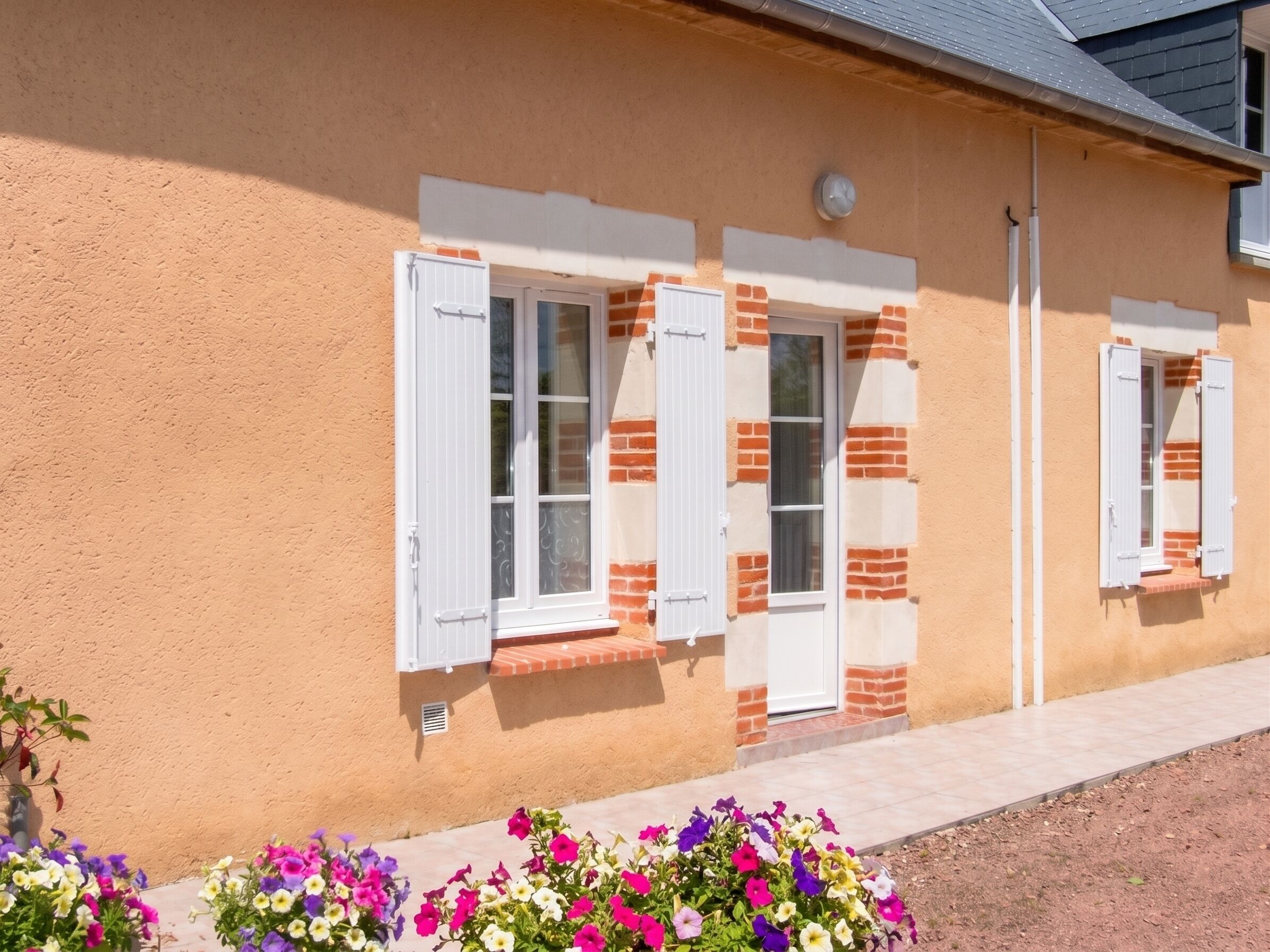 A building with a stucco exterior, white window shutters, and a brick base.