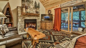 A cozy living room with a stone fireplace, leather furniture, a wooden coffee table, and a television. - River Rhapsody | Ellijay, GA (Ellijay)