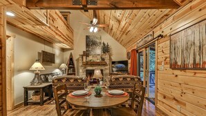 A wooden interior with a dining table, chairs, a fireplace, and a television. - River Rhapsody | Ellijay, GA (Ellijay)