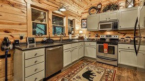 A log cabin-style kitchen with wooden walls, white cabinets, a microwave, stove, and a sink. - River Rhapsody | Ellijay, GA (Ellijay)
