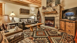 A cozy cabin interior with a fireplace, leather sofa, wooden coffee table, and a television. - River Rhapsody | Ellijay, GA (Ellijay)