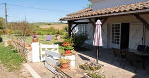 A covered outdoor seating area with a table and chairs, surrounded by potted plants and a white fence. - Homerez - House in Lannes, terrace & garden (Lannes)