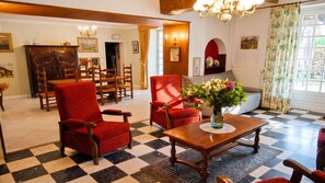 Una habitación con piso a cuadros, una mesa de madera con un jarrón de flores y un sillón rojo.