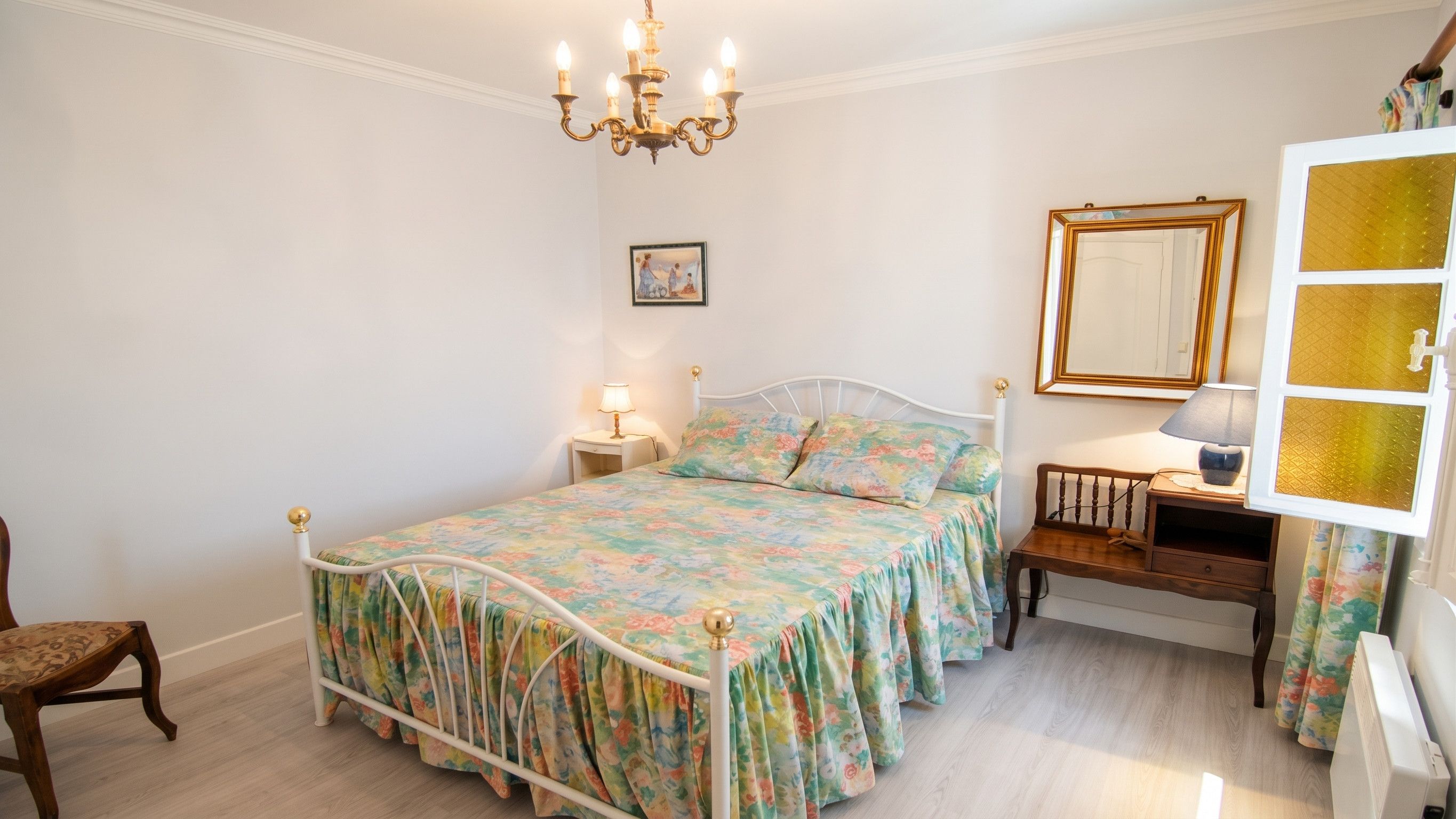 Ein Schlafzimmer mit einem Bett, einem Nachttisch, einem Sessel, einer Kommode, einem Spiegel und einer Chandelier.