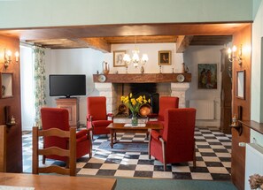 A traditional living room with a fireplace, red upholstered chairs, a television, and a checkered floor. - Homerez - House in Lannes, terrace & garden (Lannes)