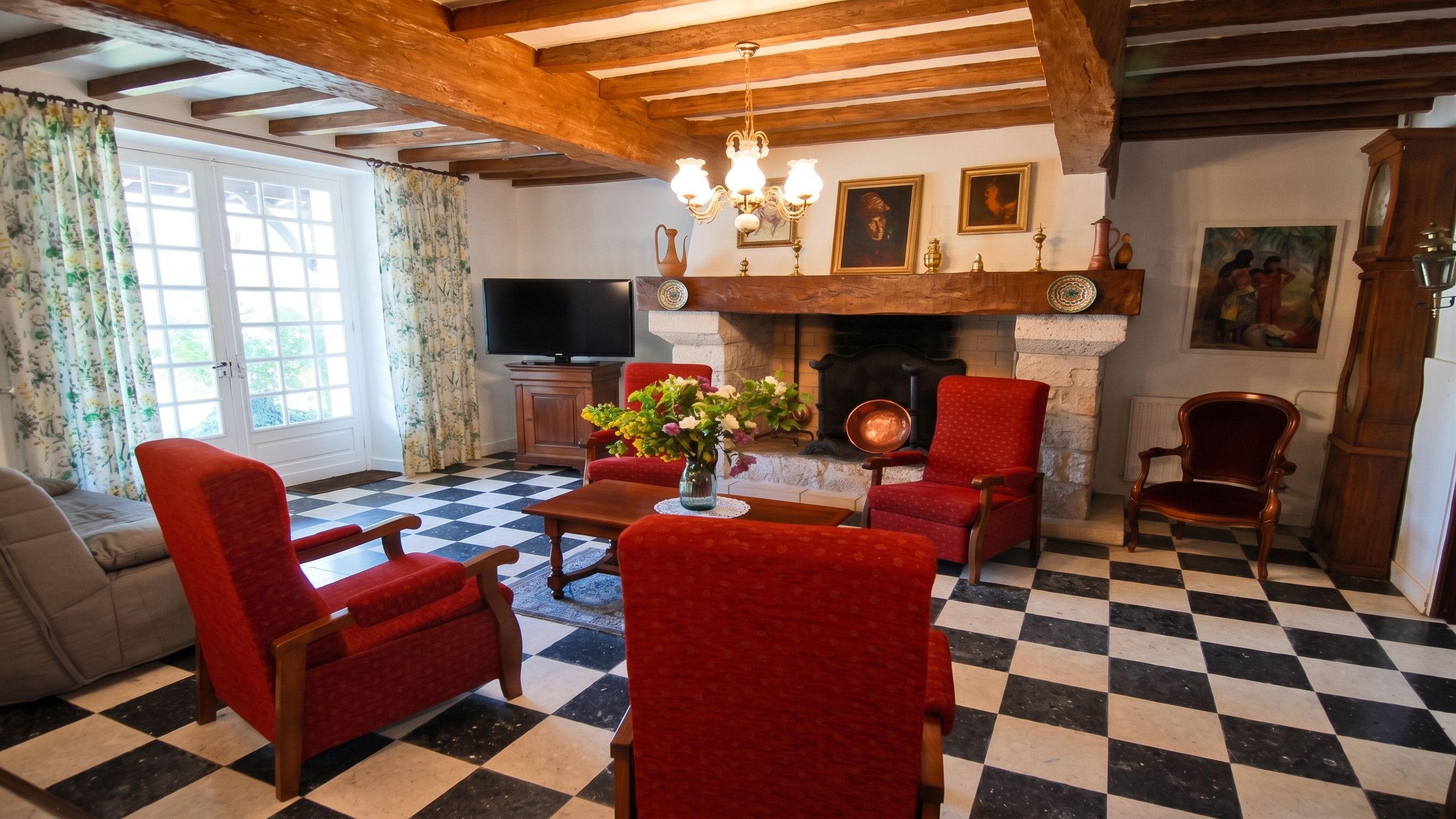 A living room with a fireplace, checkered floor, red upholstered chairs, and a television.