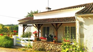 Un edificio bianco con tetto in tegole, un muro in pietra e un portico coperto con posti a sedere all'aperto.